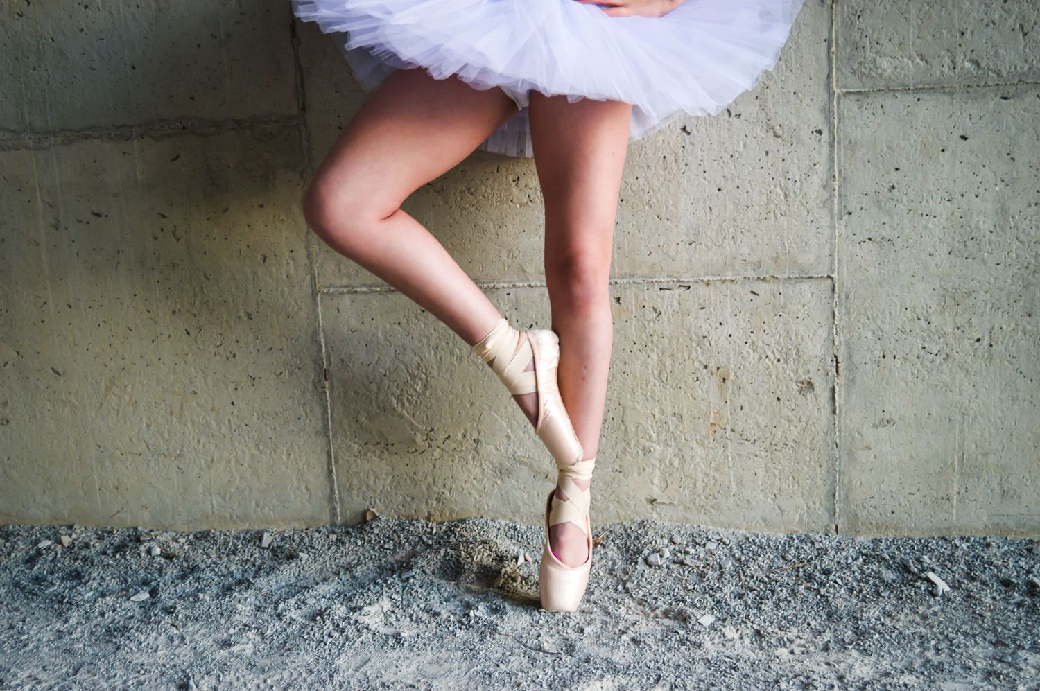 Close-up of ballet poses showing pointed feet and tutu details against concrete wall.