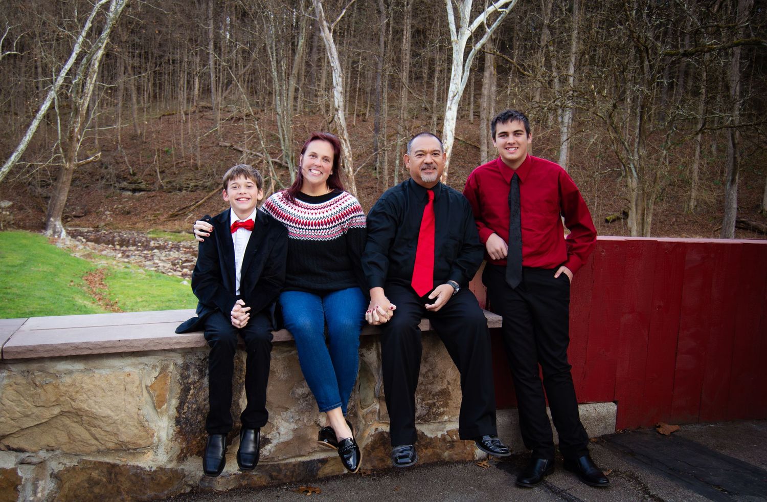 Extended family members sitting together on wooden steps outdoors against a rustic red wall backdrop.