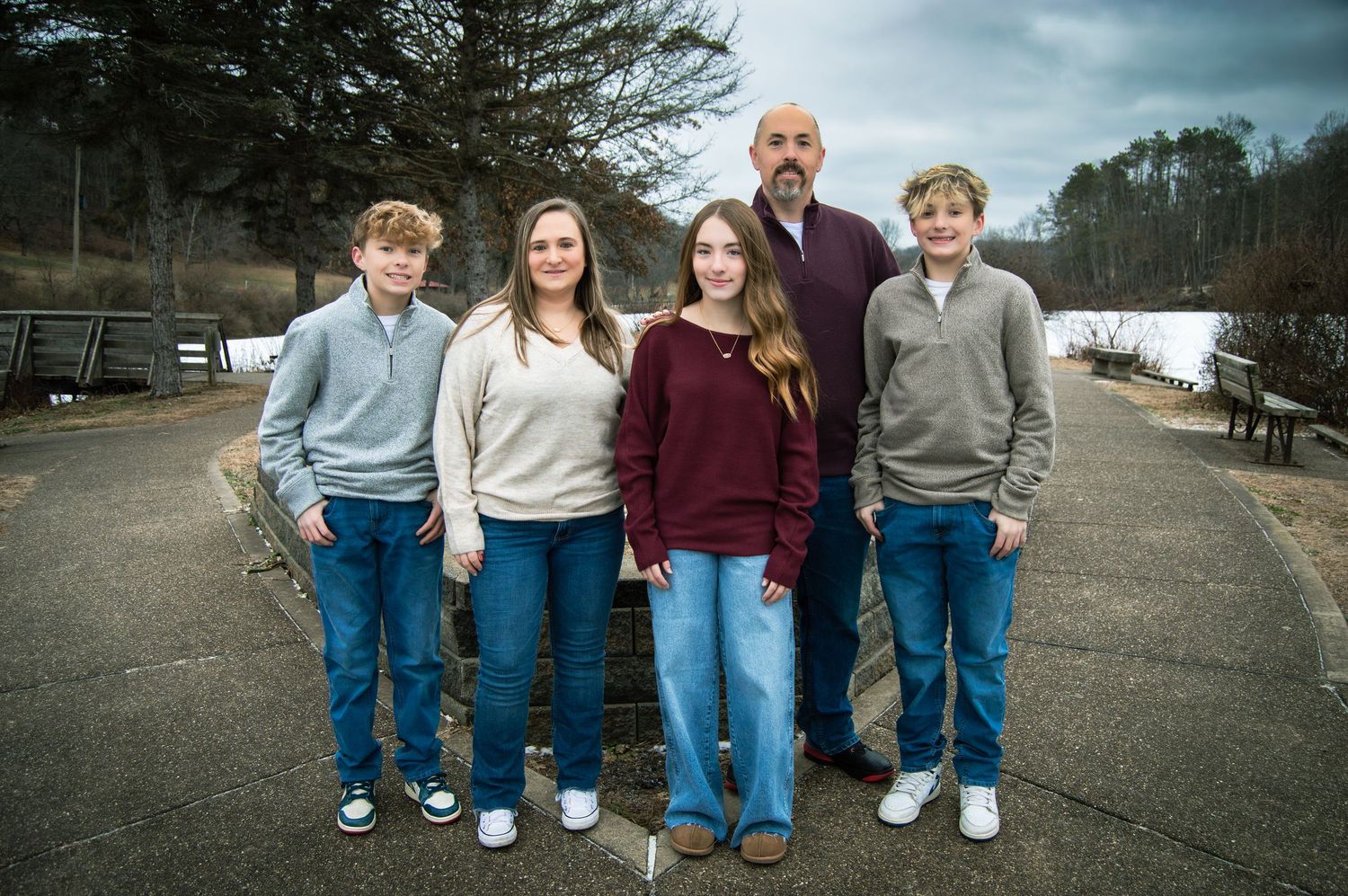 A group of four young people in casual sweaters and jeans stand together outdoors on a cloudy day.