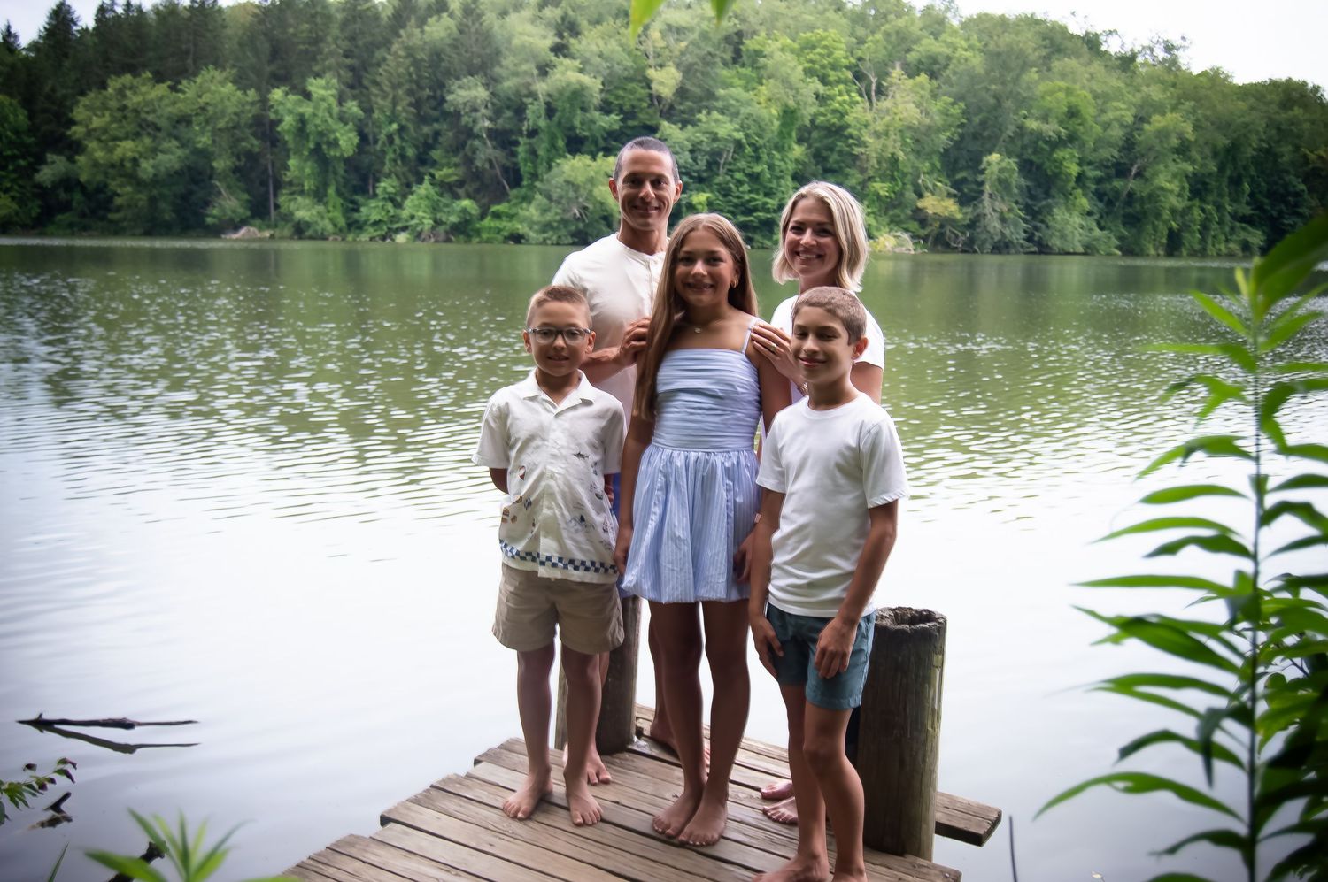 Family members gathered on a wooden dock overlooking a serene lake surrounded by forest.