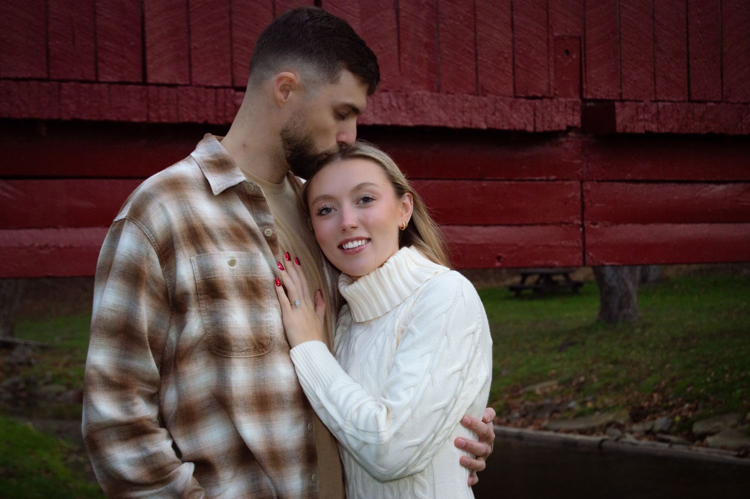 Romantic couple shares tender moment in front of rustic red barn during fall photo session.