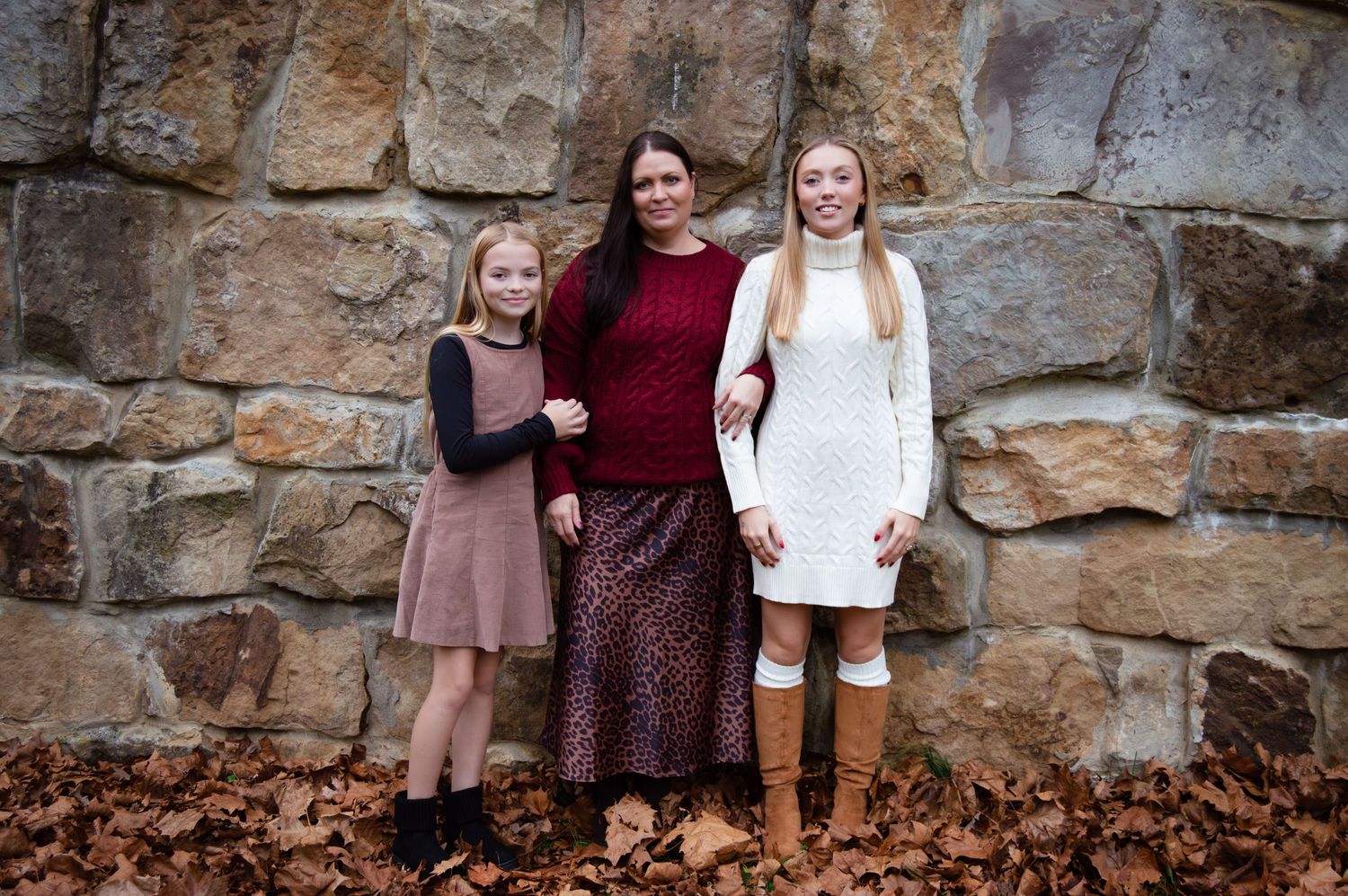 A group of people stand together smiling against a rustic stone wall background.