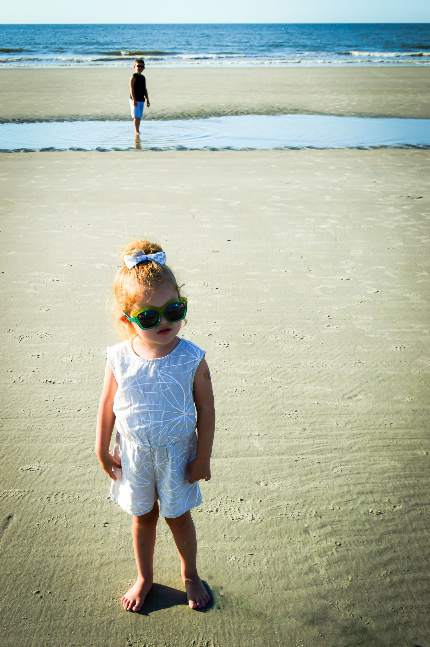 Small child exploring the sandy beach in white clothing on a sunny day.