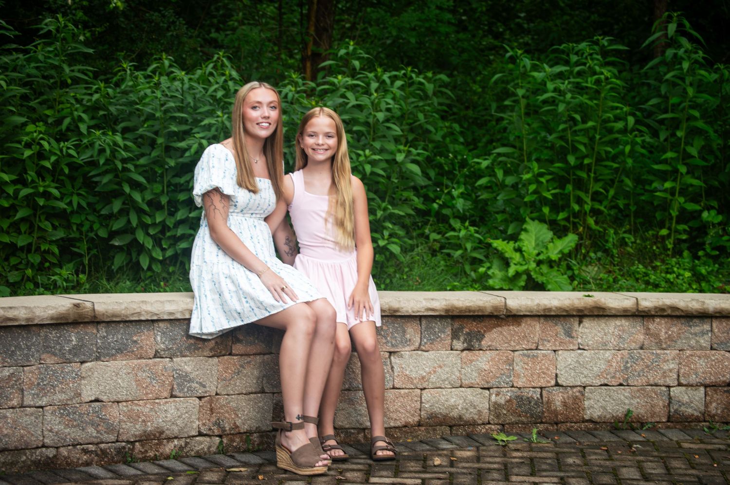 Couple sitting together on rustic stone wall surrounded by lush greenery.
