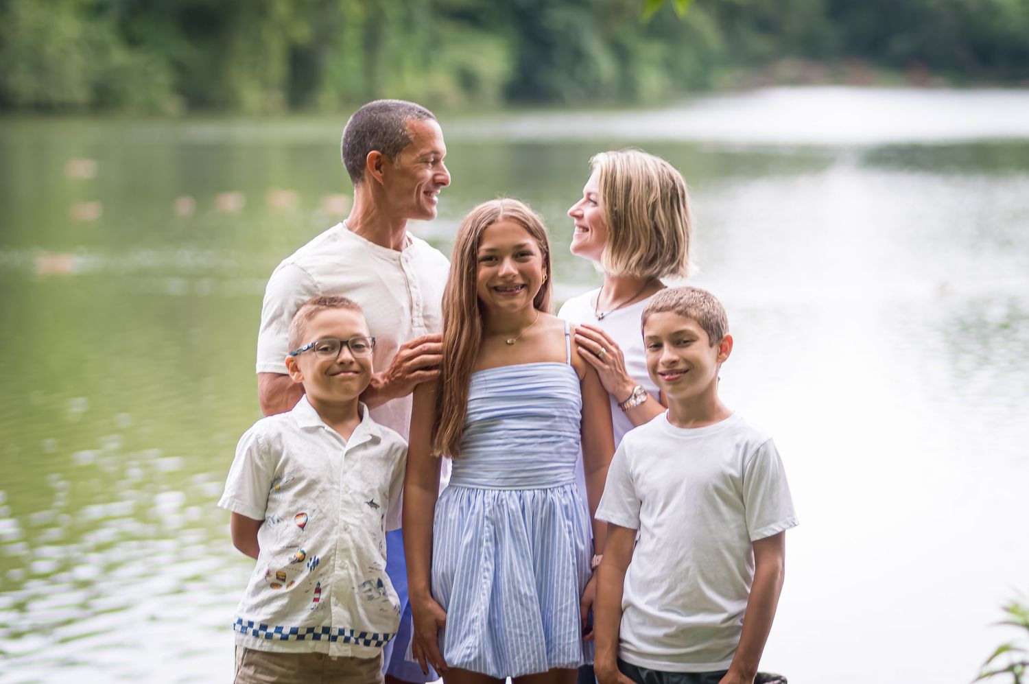 Family group poses casually by lakeside on summer day.