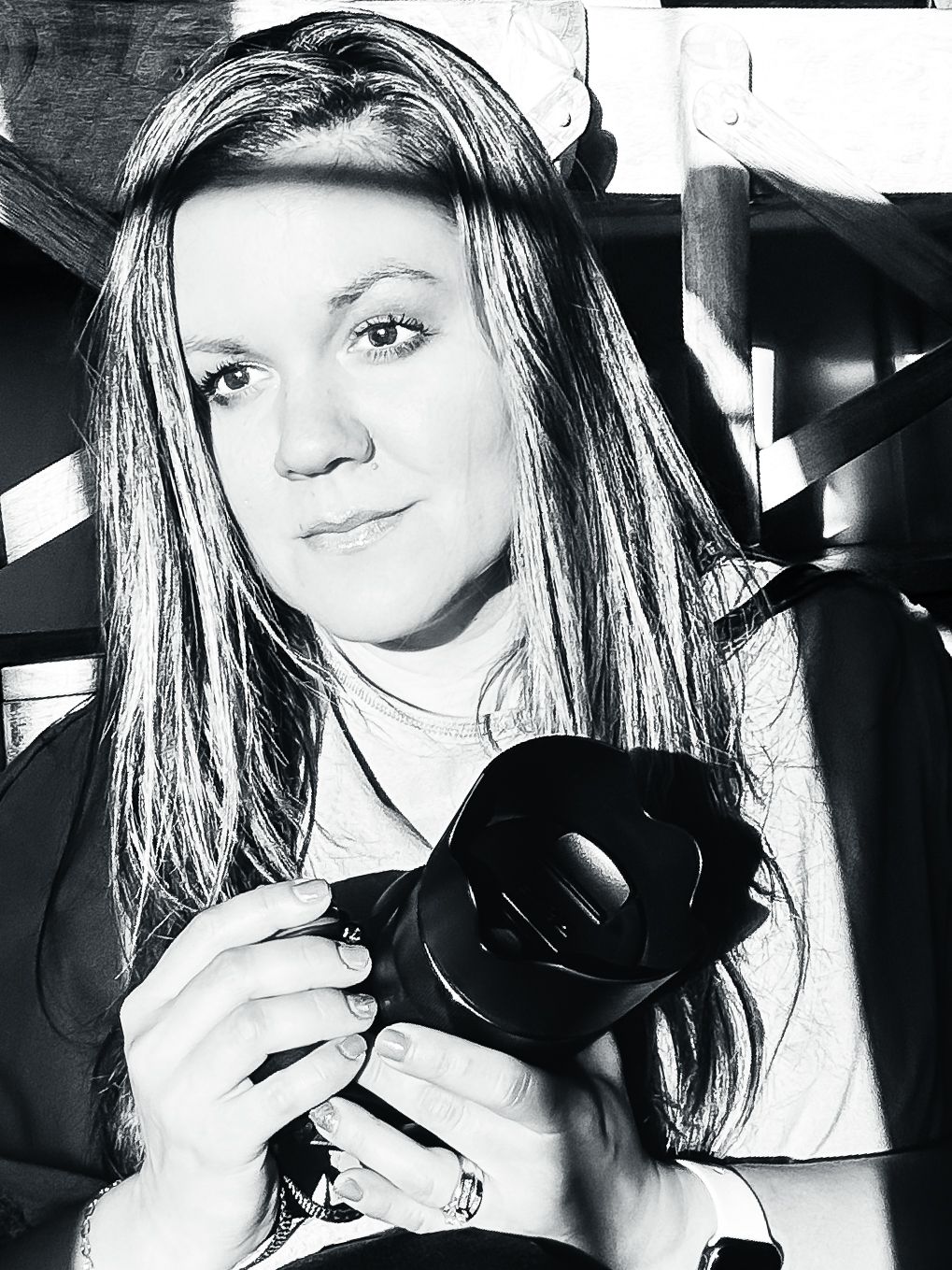 High contrast black and white portrait of photographer with long hair holding camera.