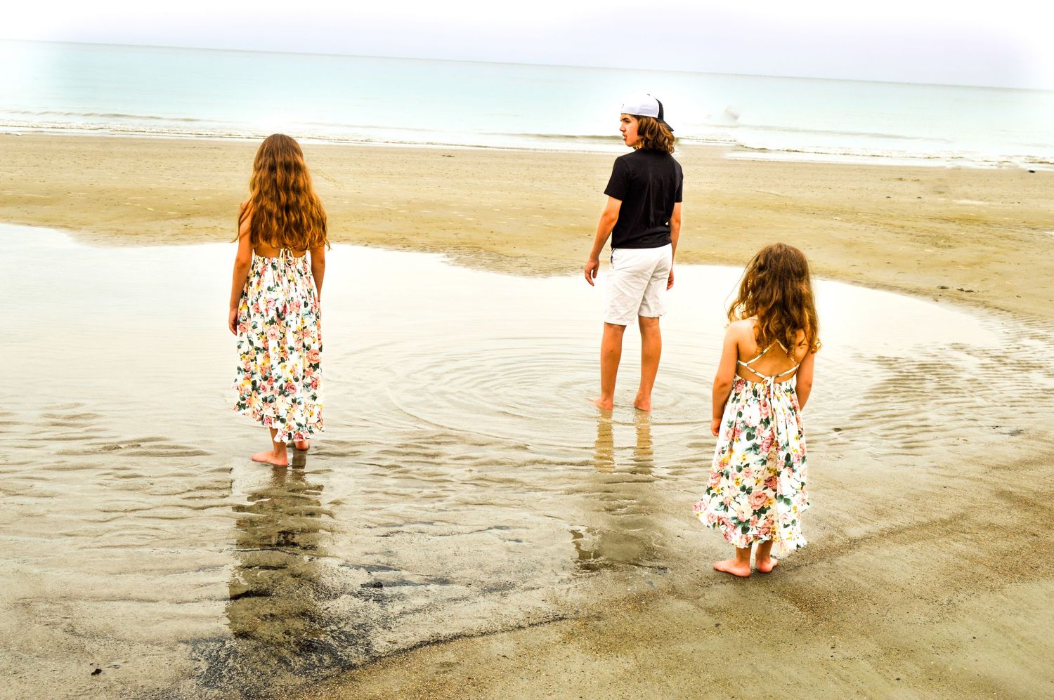 Small group walking through gentle waves on a serene beach at dusk.