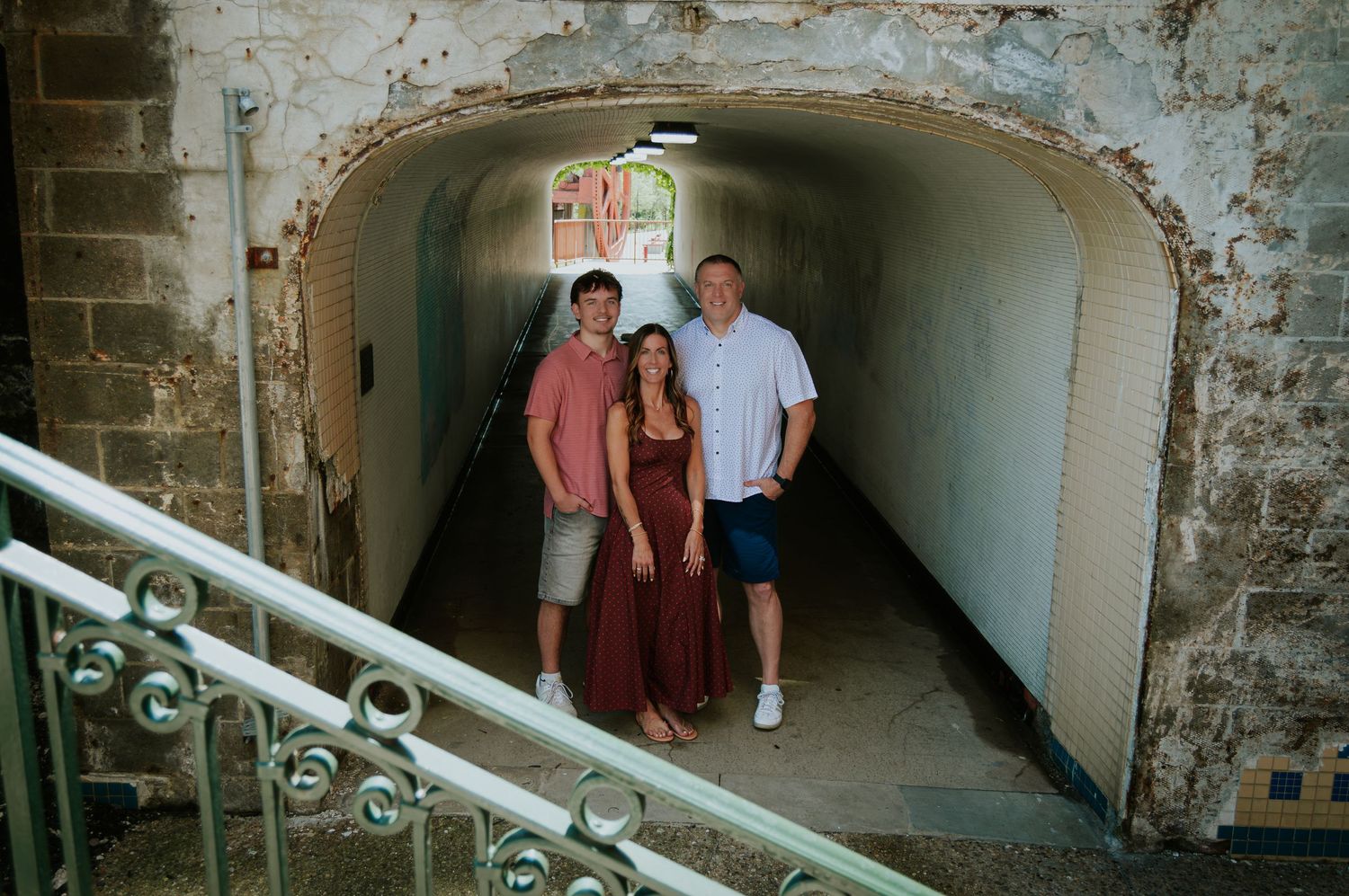 Three people posing together in a rustic stone tunnel archway with stairs nearby.