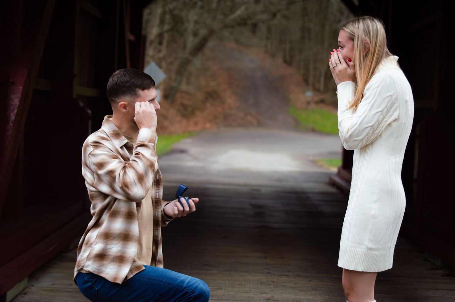A romantic proposal moment captured on a covered bridge with someone kneeling and holding a ring.