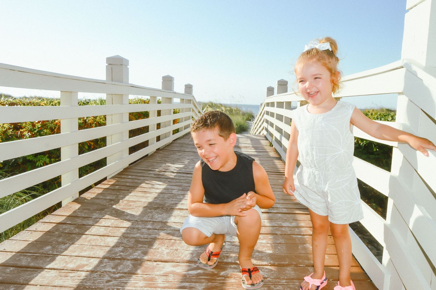 Child playing and crawling on a wooden boardwalk at the beach on a sunny summer day.