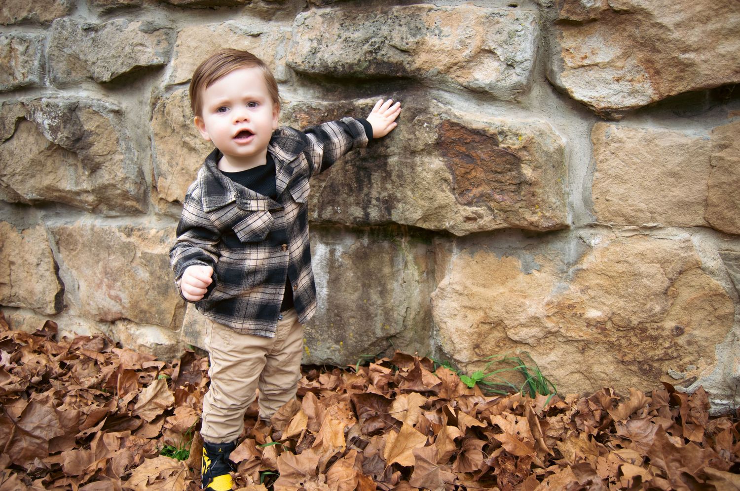 Child playing near a rustic stone wall with autumn leaves scattered on the ground.