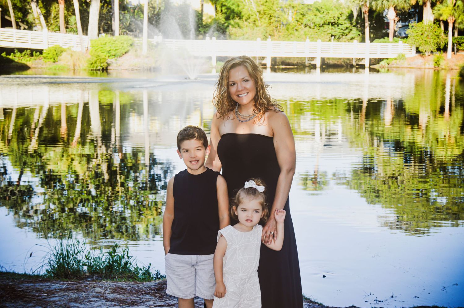 Family group photo taken by a serene lake with trees reflecting in the calm water.
