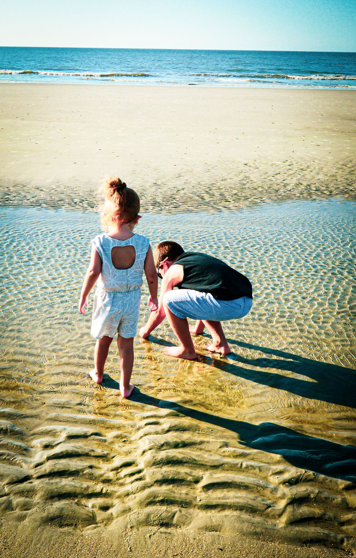 Two people explore the wet sand at the beach's edge during low tide.