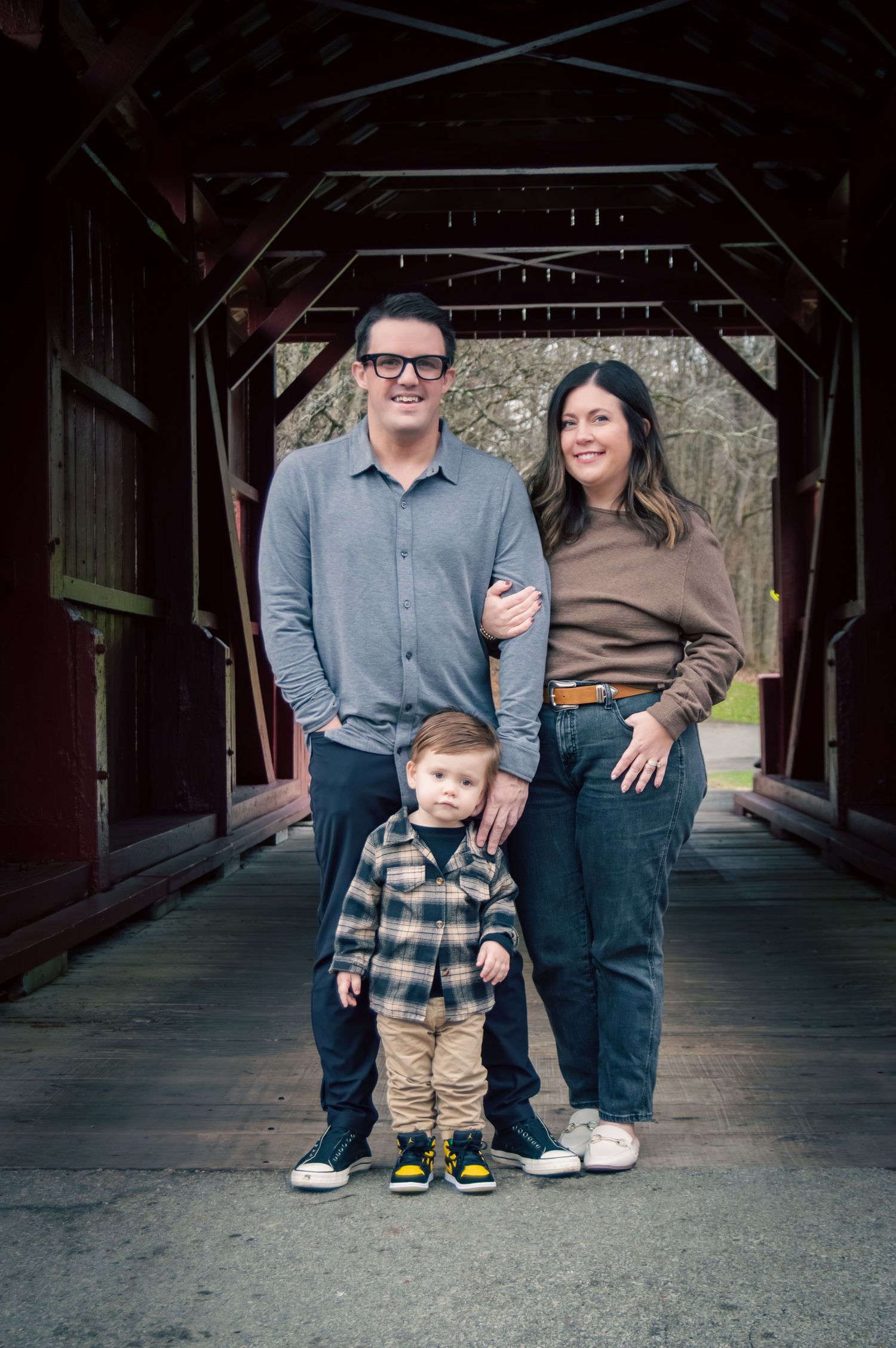 A family poses together on a covered wooden bridge in casual attire for outdoor portraits.