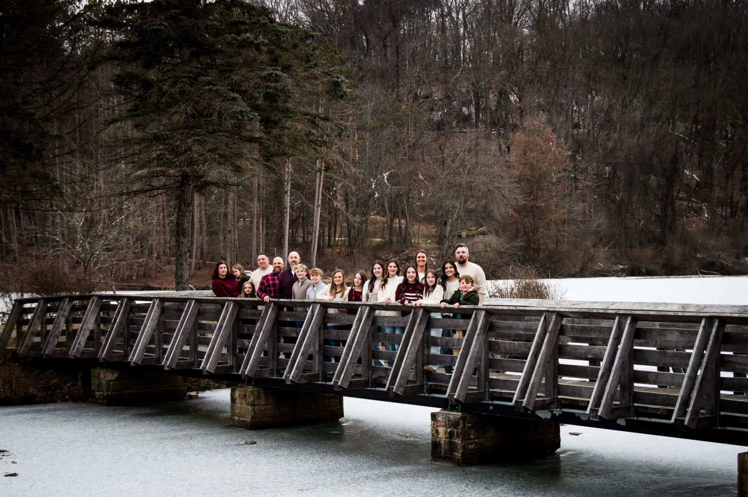 A panoramic view of a wooden bridge crossing a lake with bare winter trees in the background.