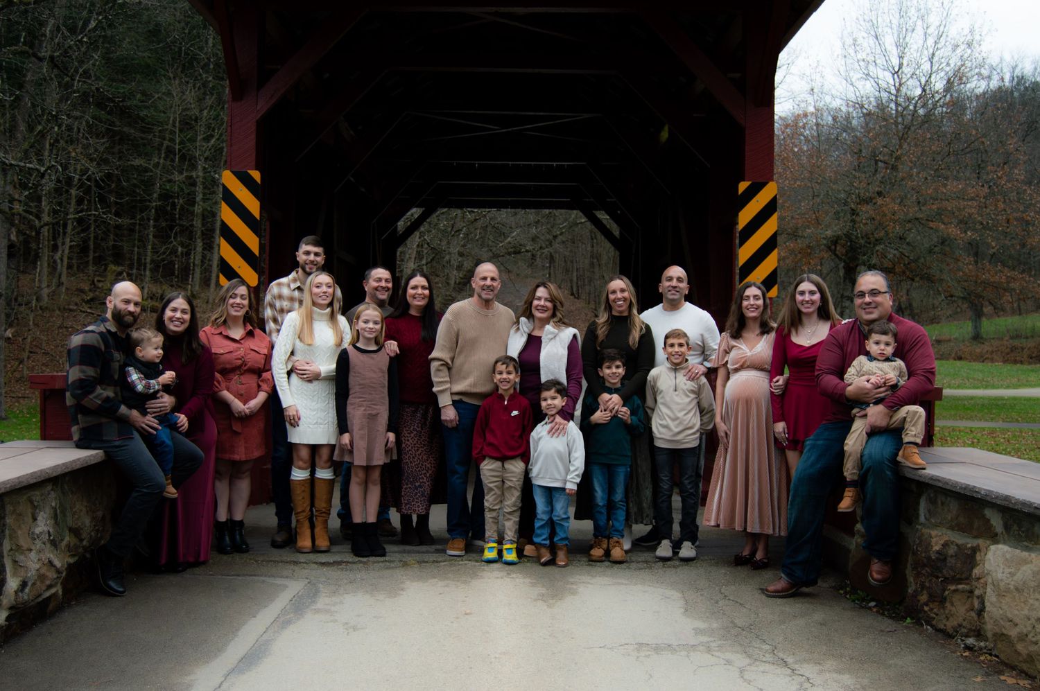 Large group of people in coordinated burgundy and neutral attire posing outdoors for formal photos in a park setting.