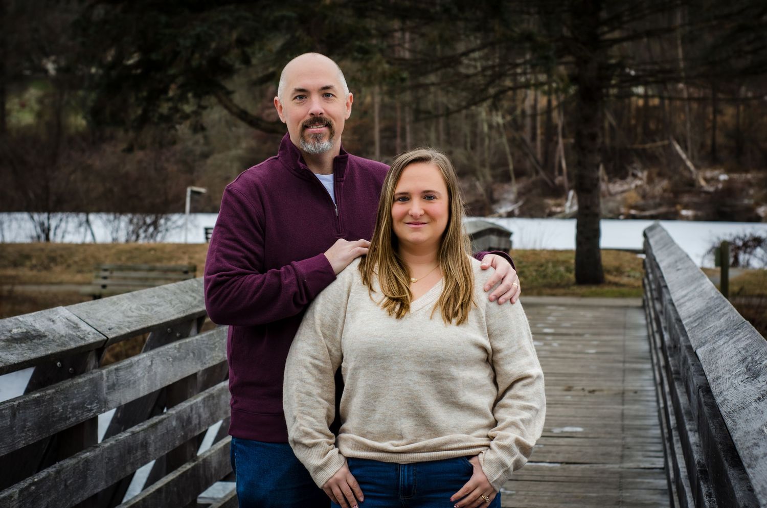 A couple in coordinating cream and burgundy outfits share intimate moments on a wooden boardwalk during an autumn photo session.