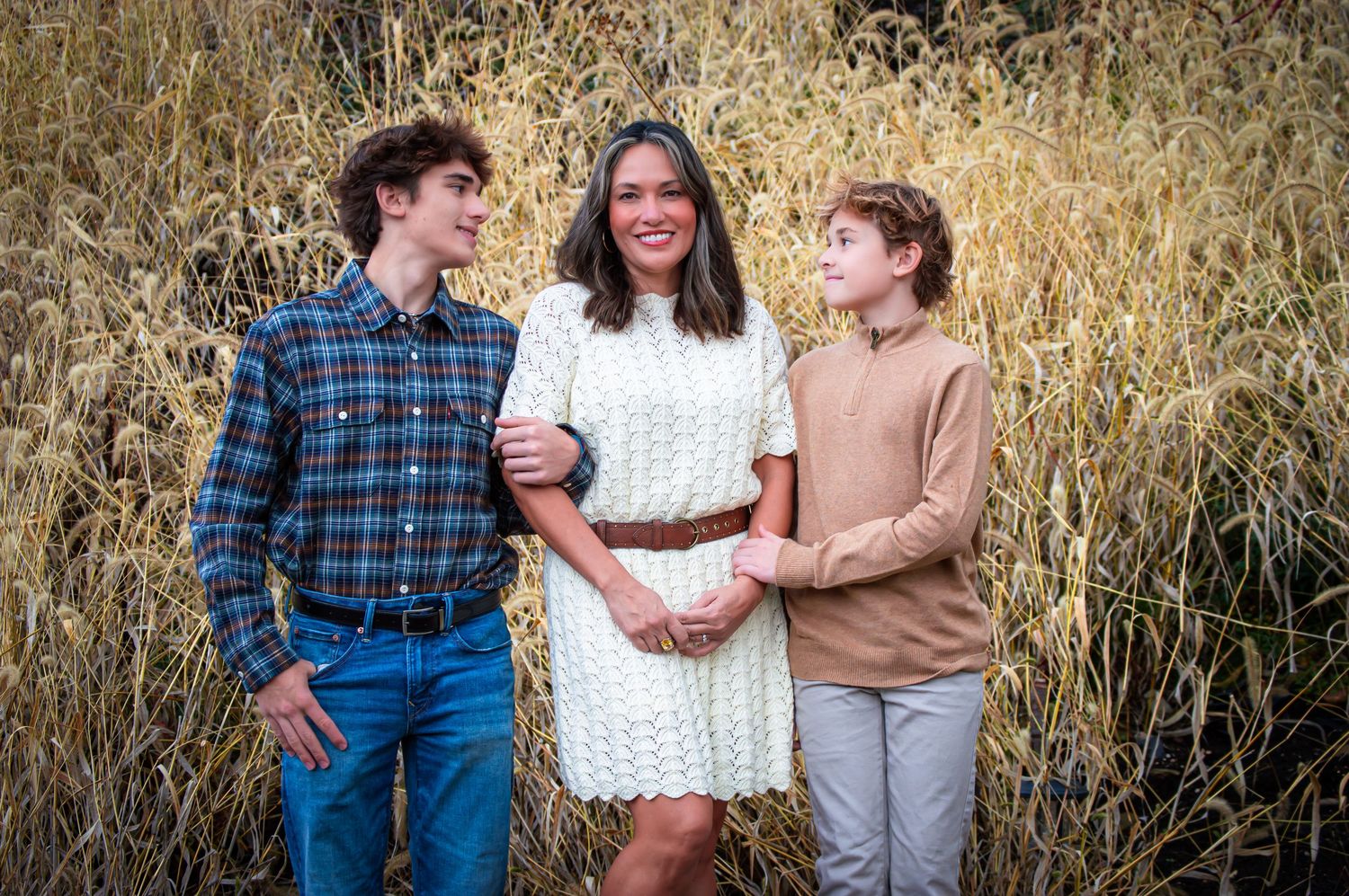 Three people pose casually in front of tall dried grass on a sunny day.