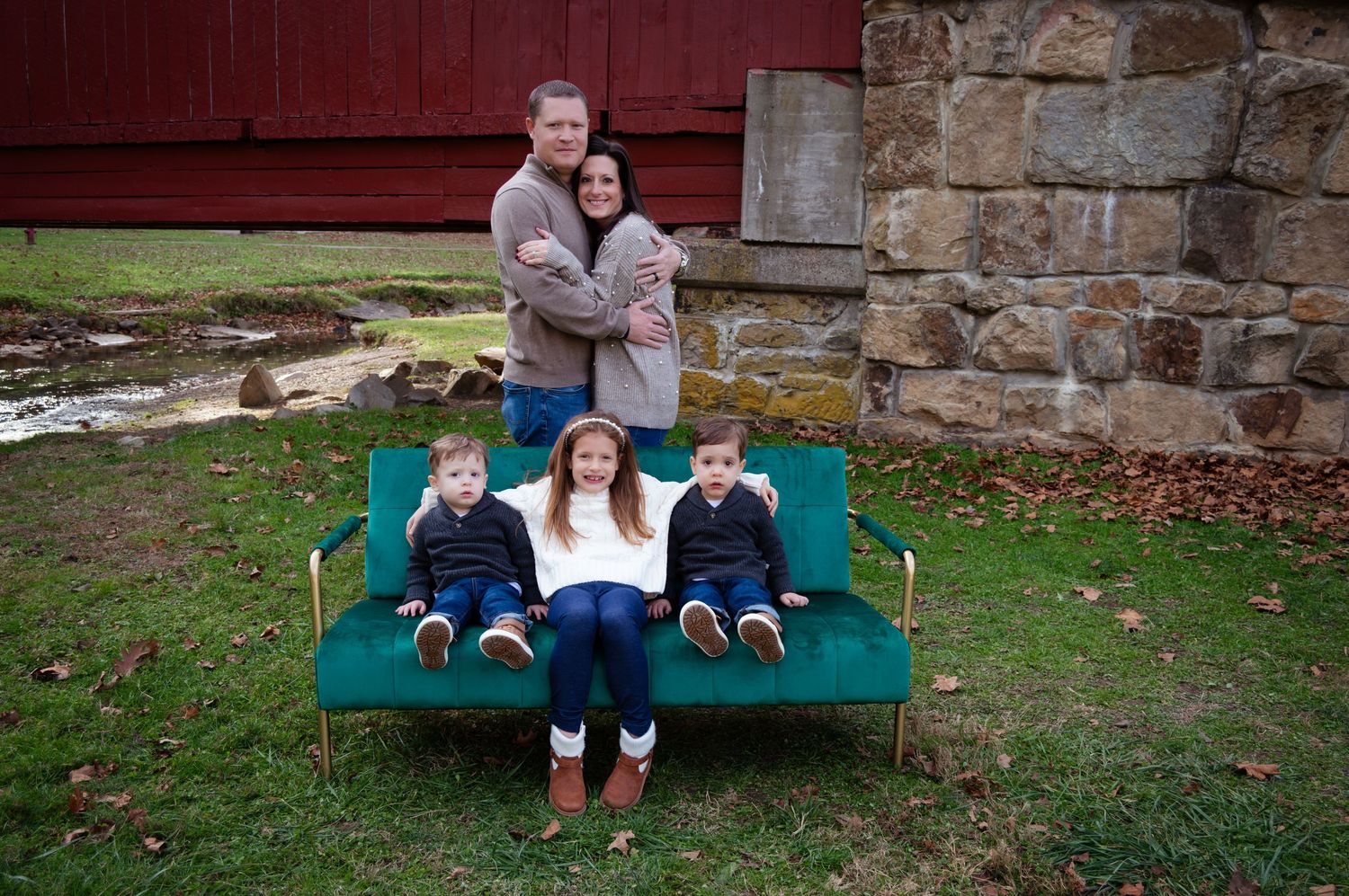 People sitting together on a green bench against a stone wall in an outdoor setting.