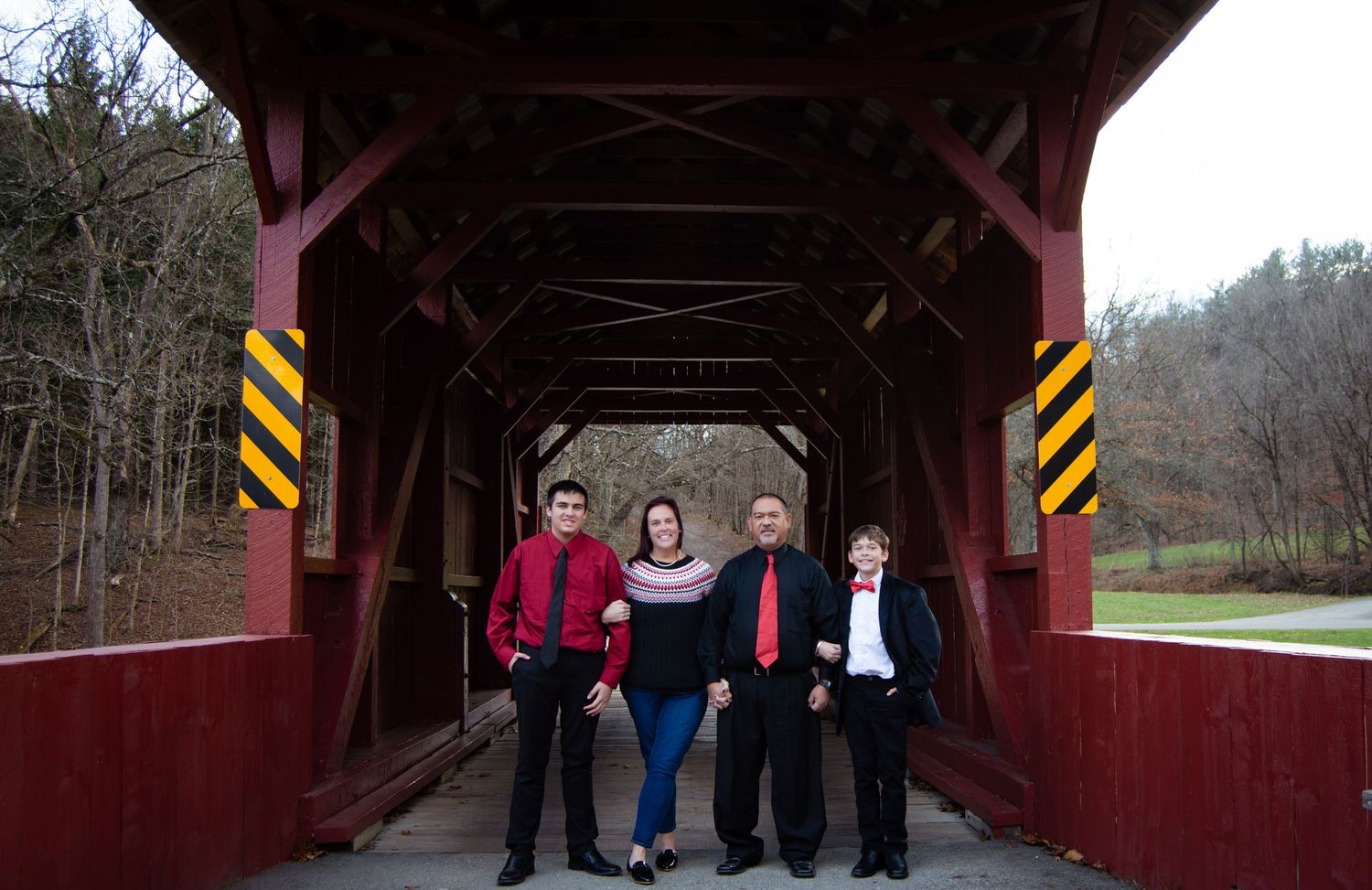 A group of people walk through a rustic red covered bridge on a sunny winter day.