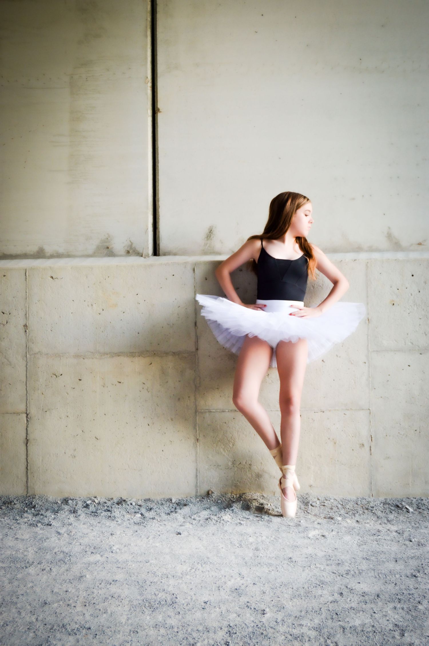 Ballet dancer in white tutu performs elegant poses against industrial concrete backdrop.