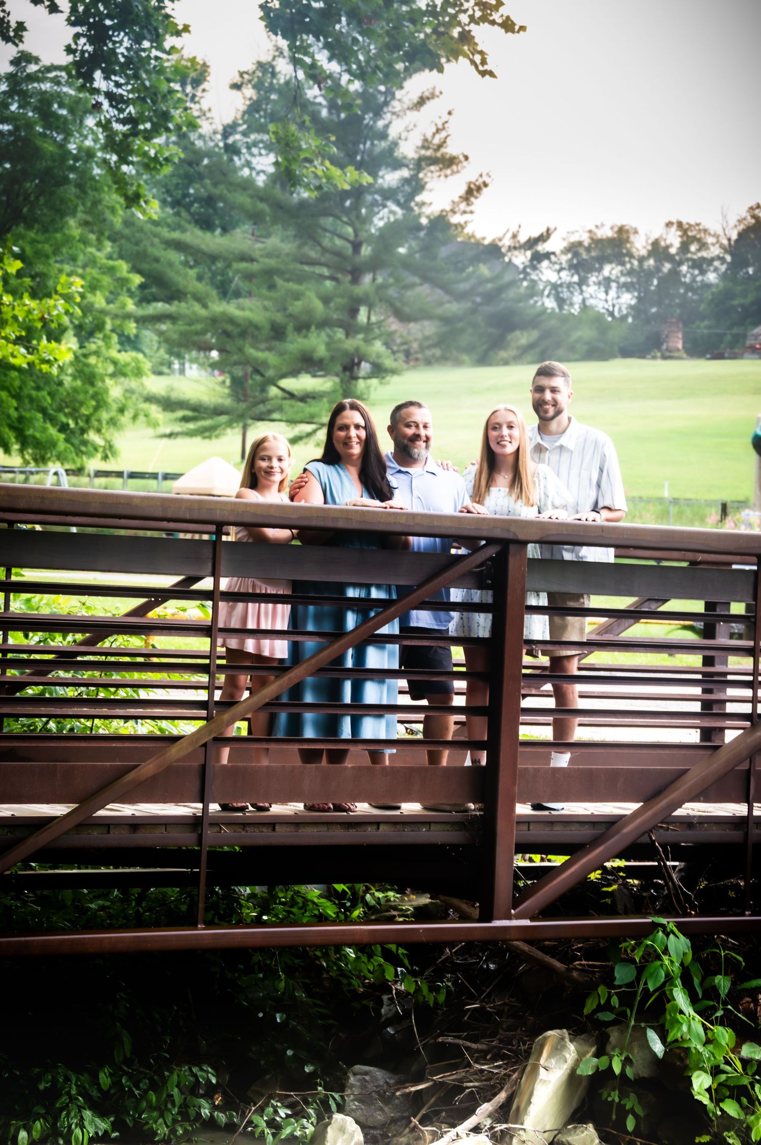 Group photo of people standing on wooden bridge overlooking green golf course.