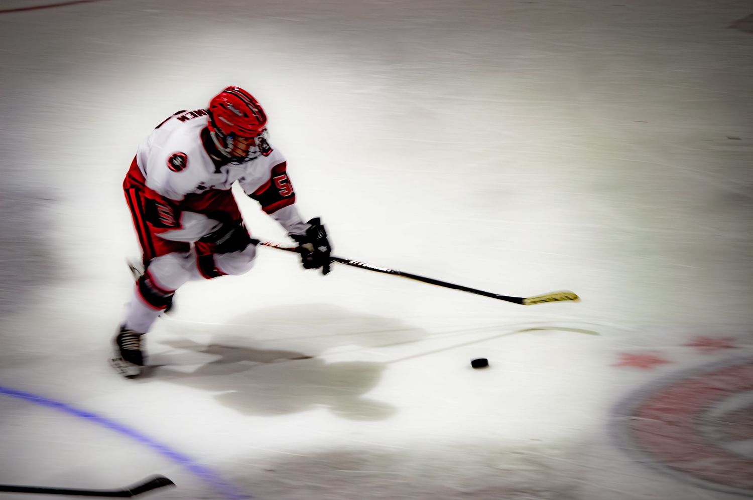 Hockey player in red uniform practicing puck control drills on ice.