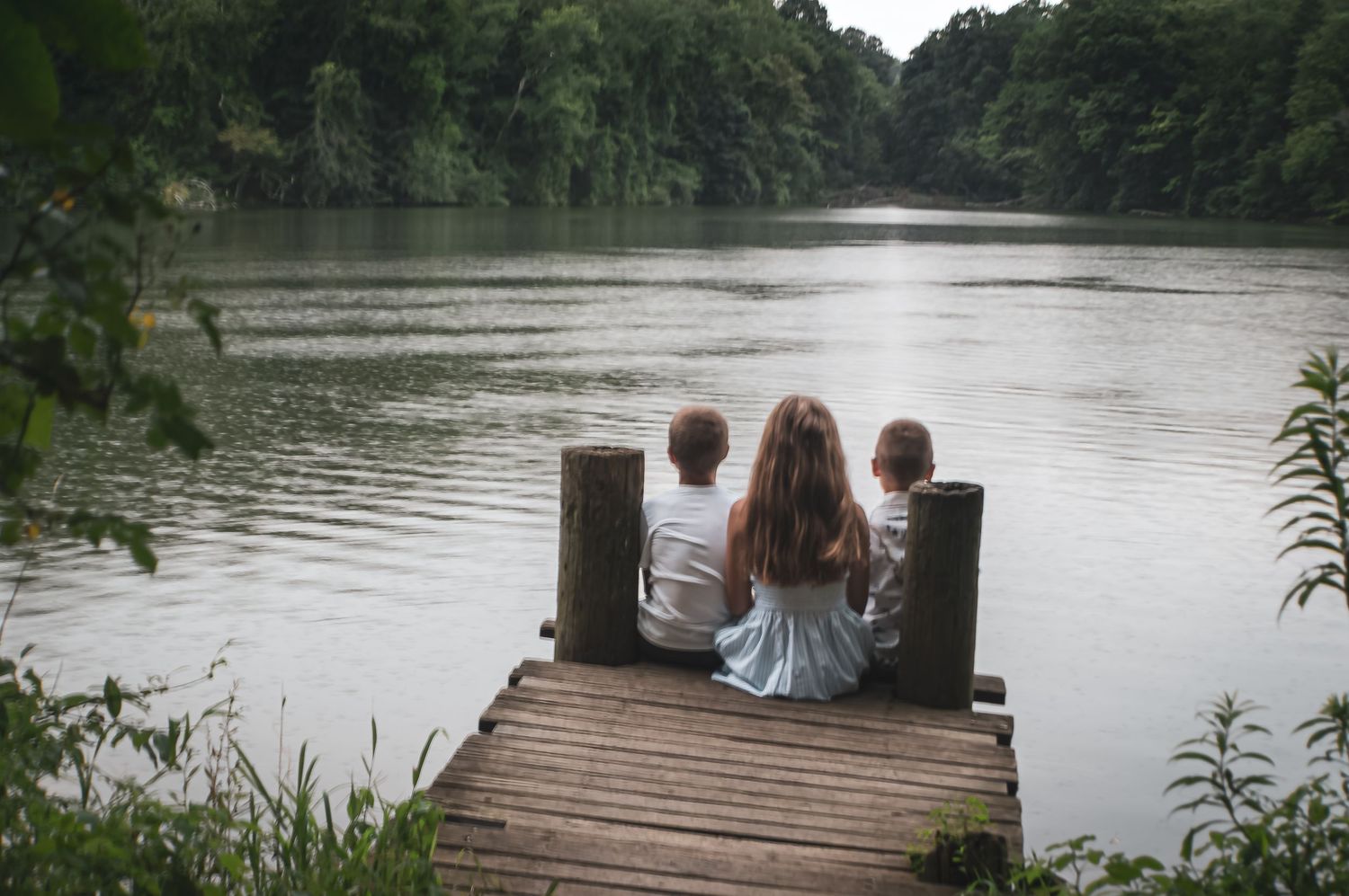 People sitting together on a rustic wooden pier extending into a tranquil lake on a summer day.