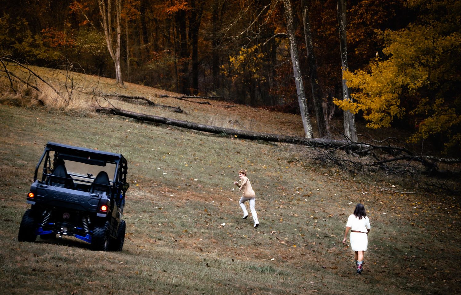 A vintage car drives along a scenic autumn road through golden foliage and fallen leaves.