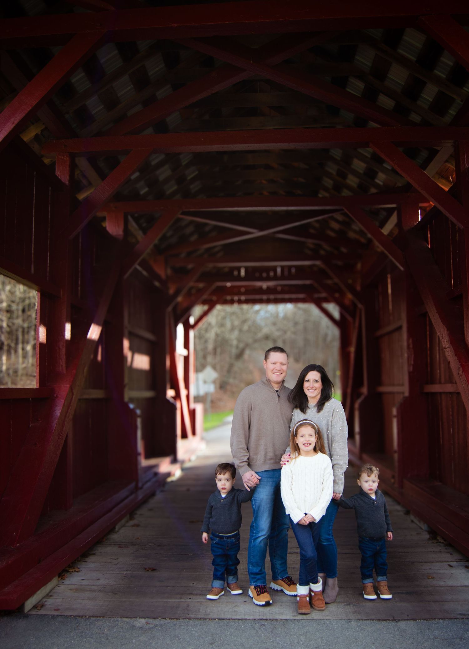 A family poses together inside a rustic red covered bridge with natural light streaming through the openings.