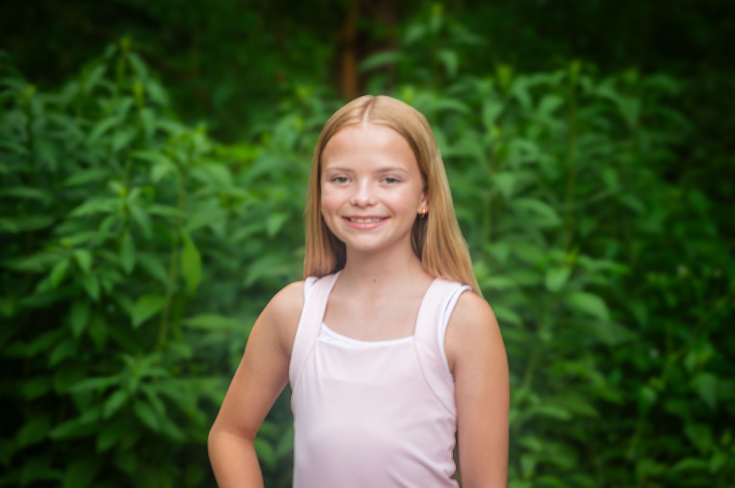 Portrait of someone in a pink tank top smiling against greenery.