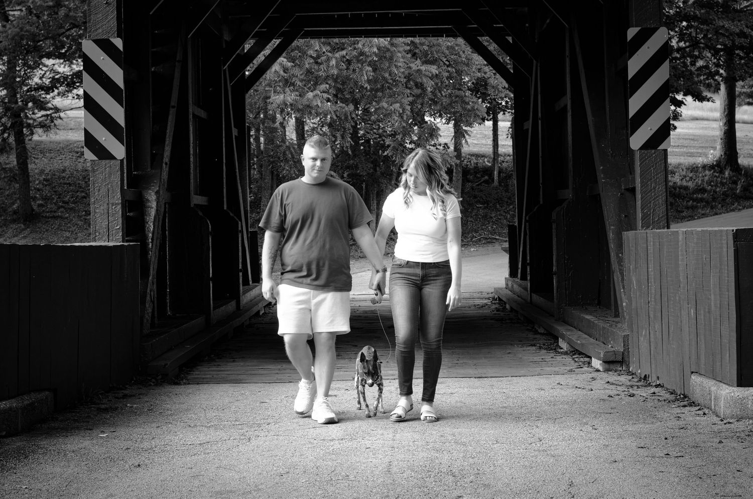 Couple walking hand in hand through a rustic covered bridge in black and white photography.