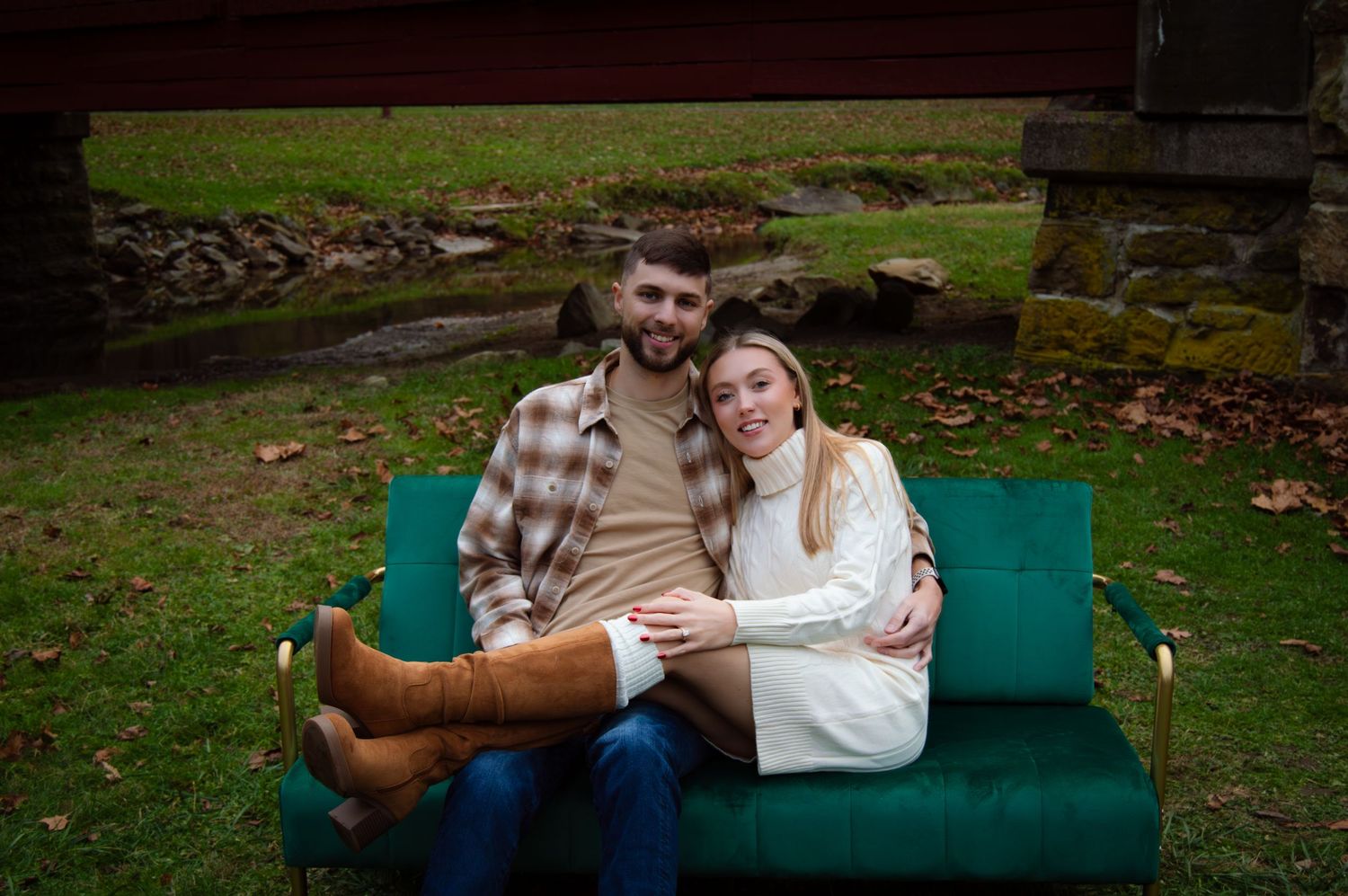 A couple sits close together on a teal-colored couch outdoors surrounded by autumn foliage.