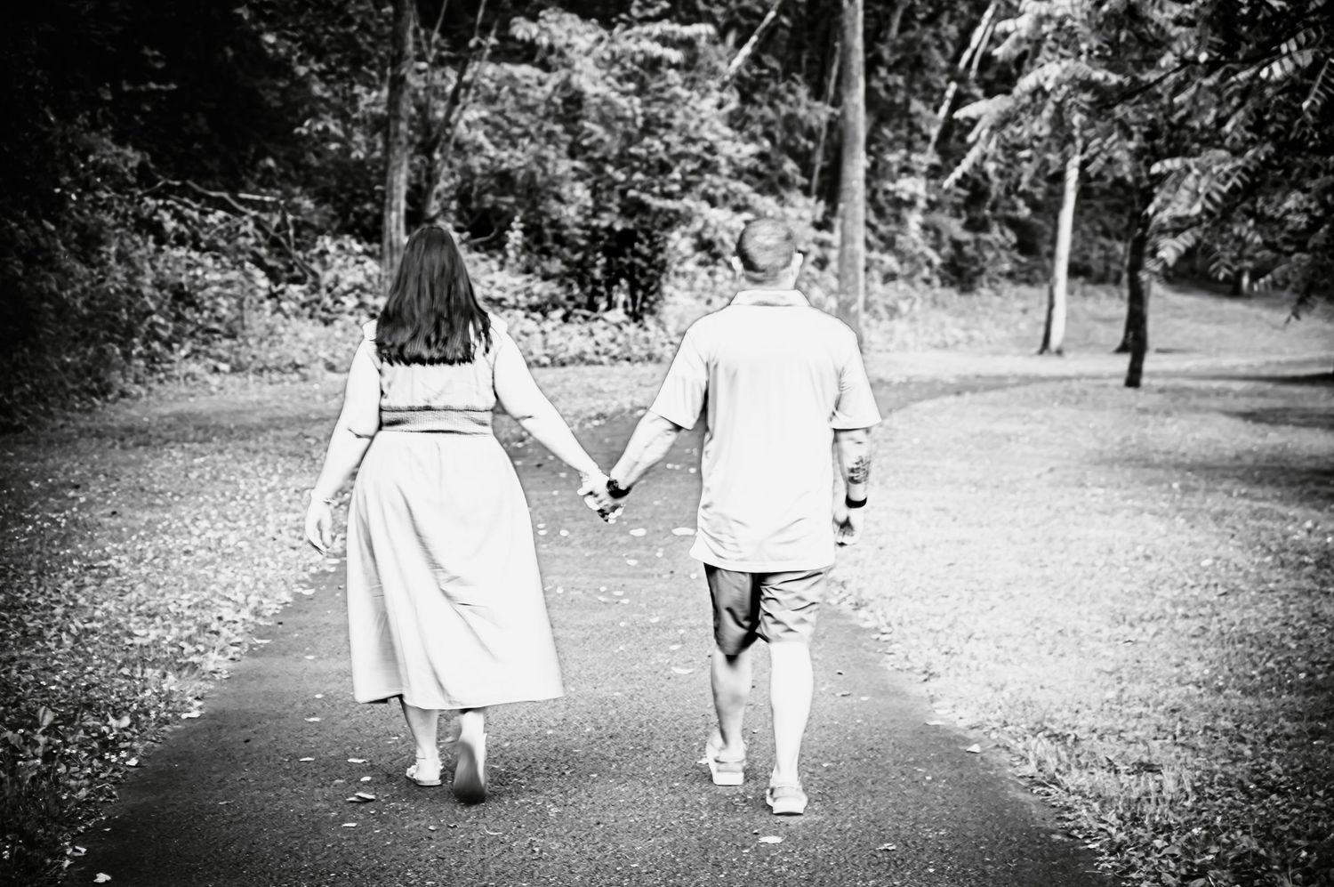 Black and white image of a couple walking hand in hand down a tree-lined path.