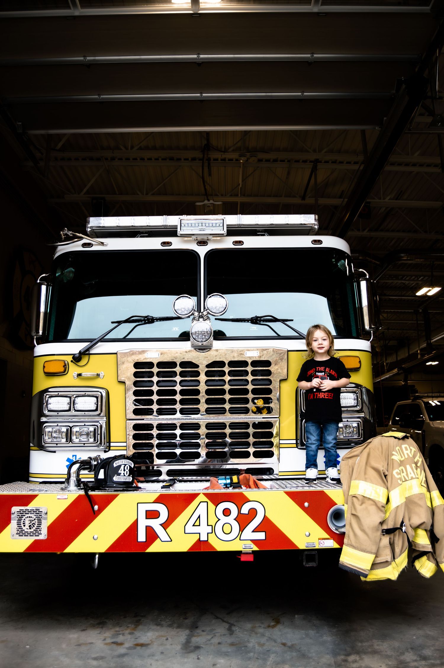 A yellow fire truck with number R482 is parked in a station bay with firefighting gear visible in the foreground.