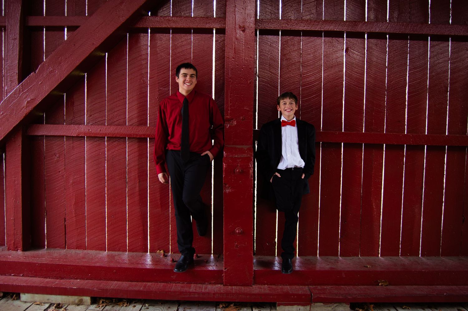 A group of people stand in front of a large red wooden barn structure at dusk.