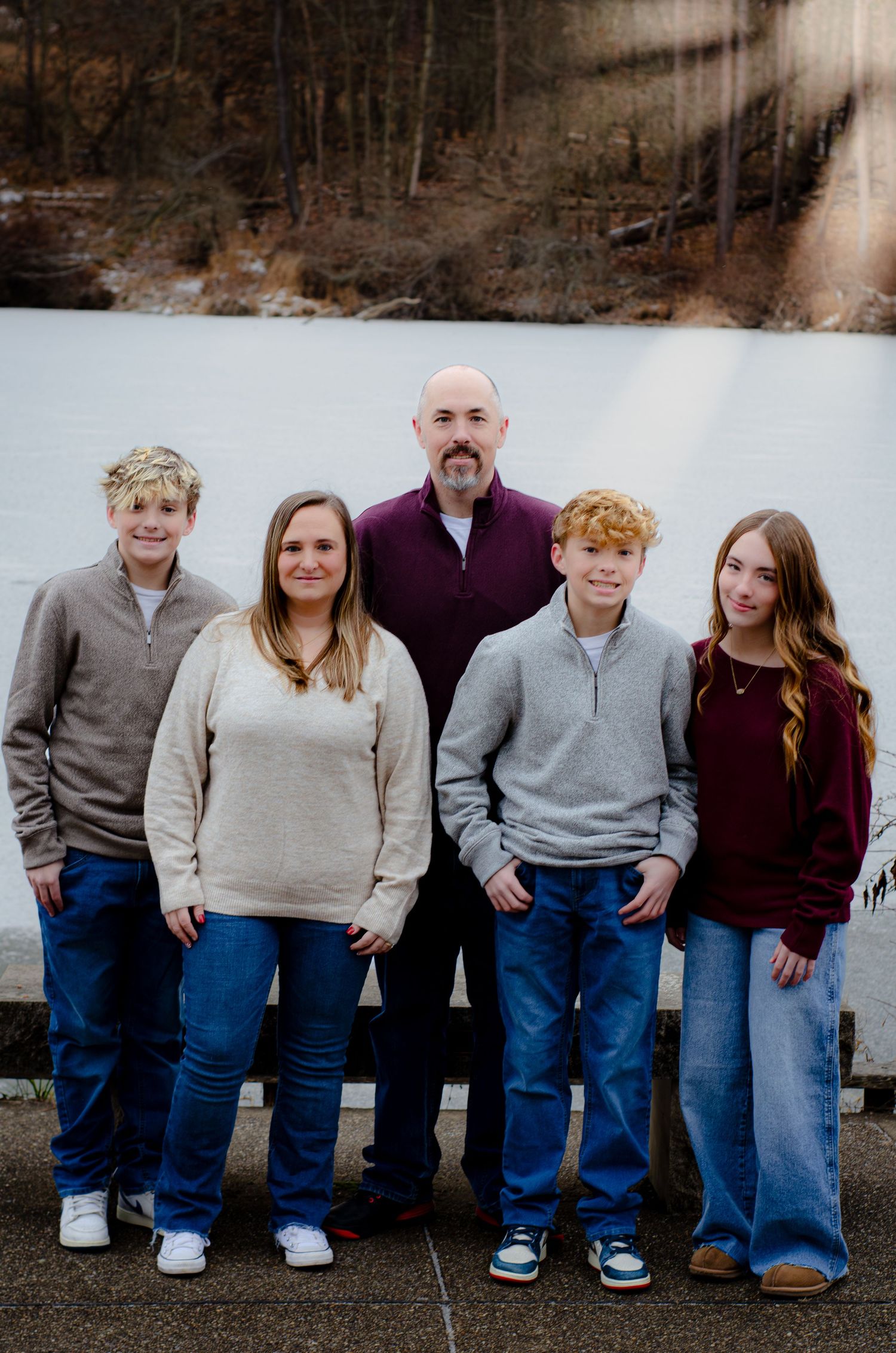 A family sits together outdoors wearing coordinated outfits of jeans and sweaters on a winter day.