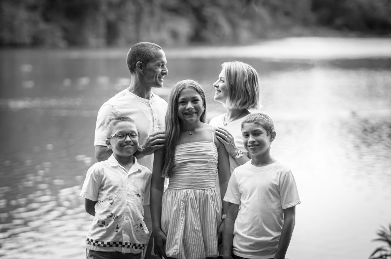 Black and white family portrait by a lake showing four people smiling together.