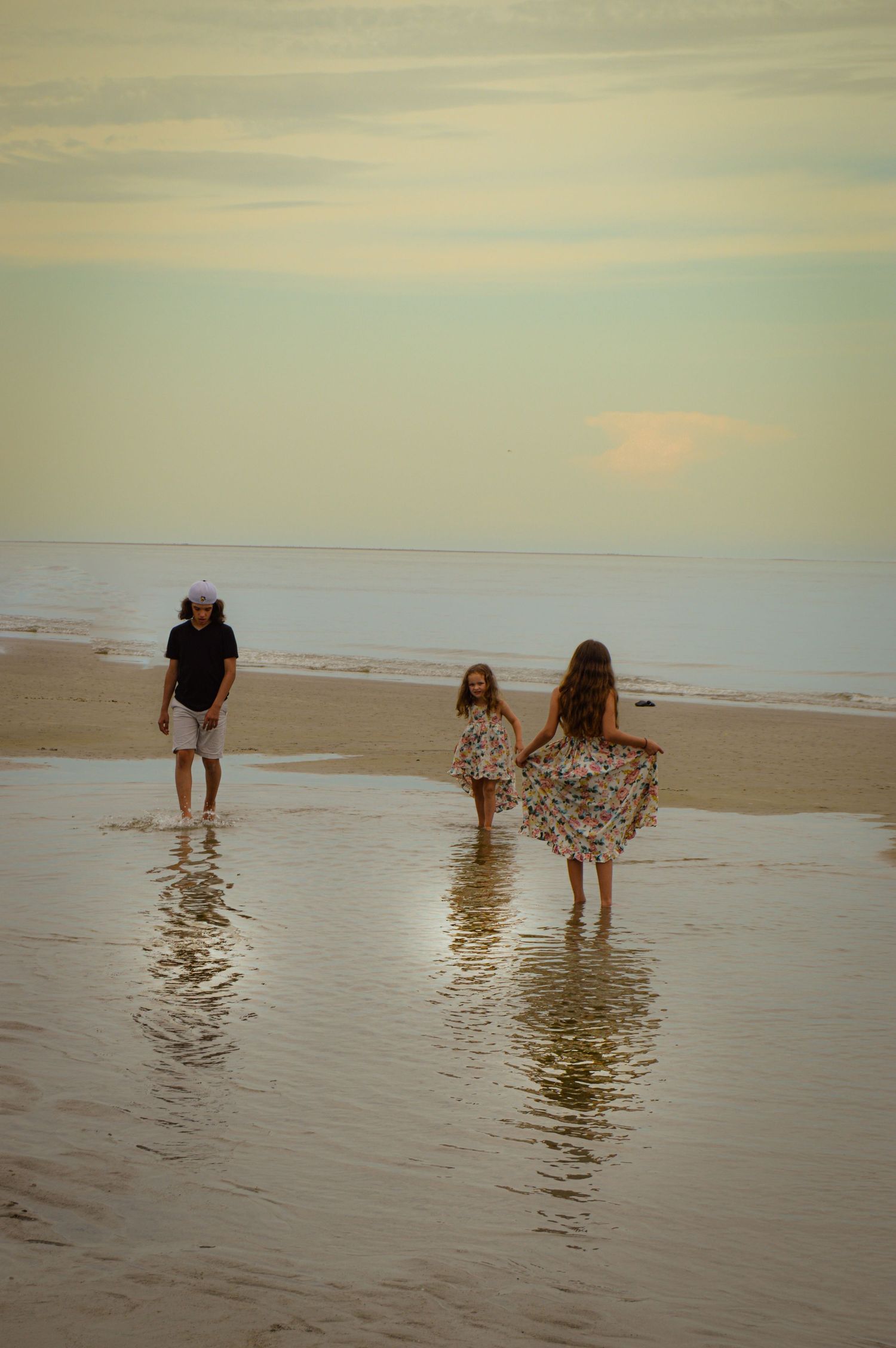 People wading in shallow ocean water at sunset on a peaceful beach.