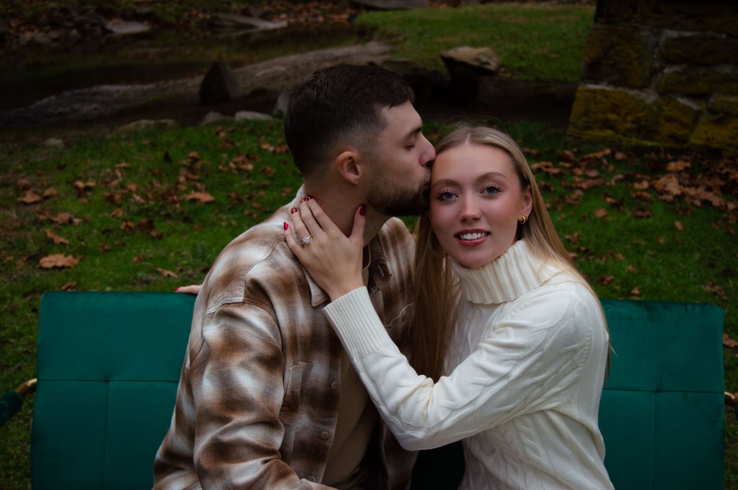 A couple in warm sweaters share romantic moments on a green park bench during autumn.