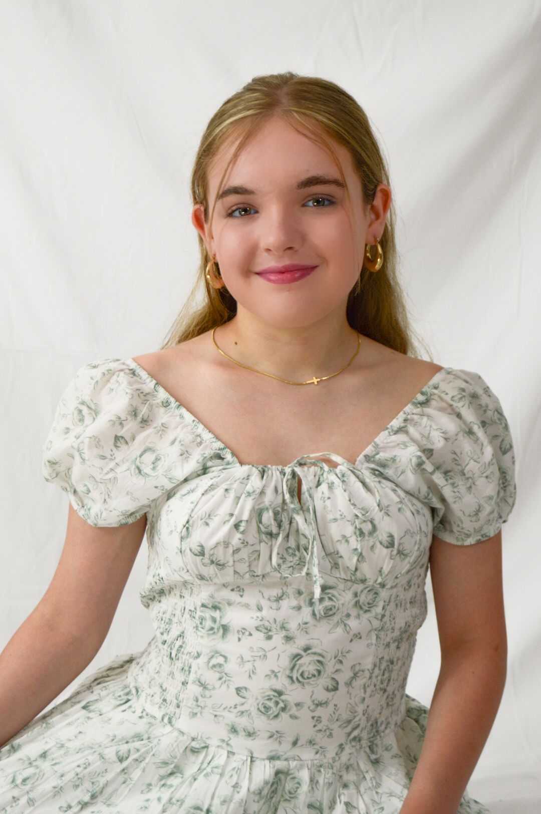 Young woman in vintage-style white and green floral dress with puff sleeves poses against white backdrop.