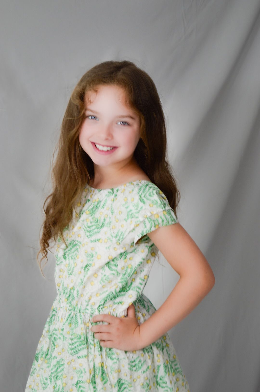A series of four photos showing a child in a floral green and white dress posing against a gray backdrop.