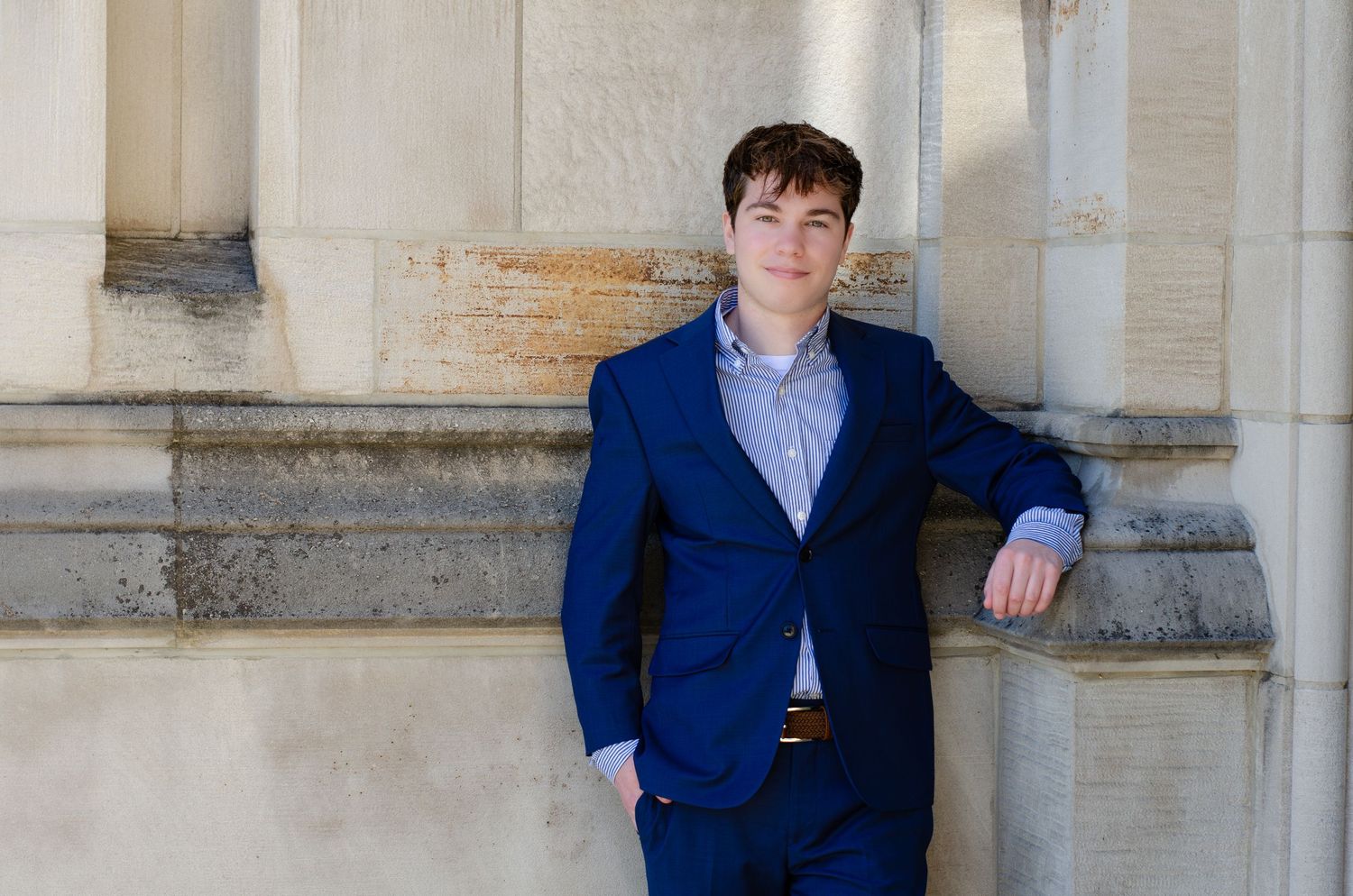 Young man in blue suit posing confidently against stone columns for a professional portrait photo.