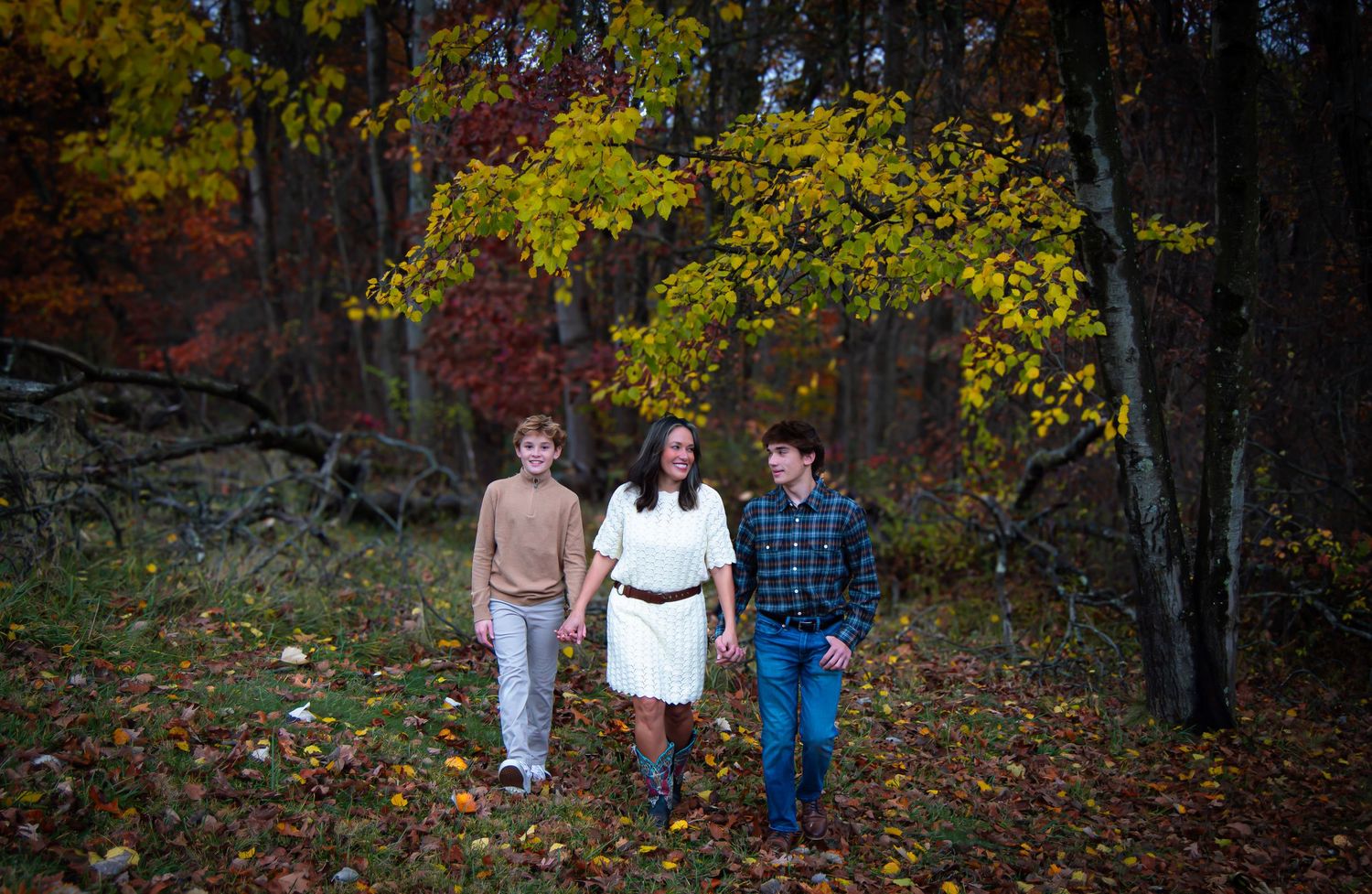 A family walks through a colorful autumn forest during a fall photo session.