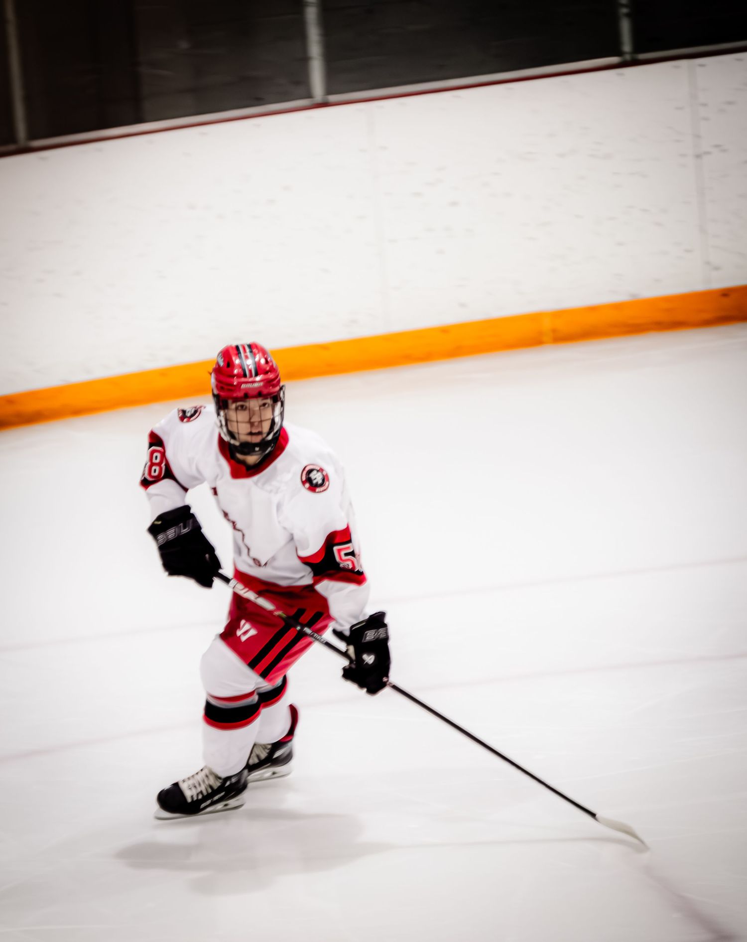 A hockey player in red and white uniform glides across the ice in a dynamic skating motion.