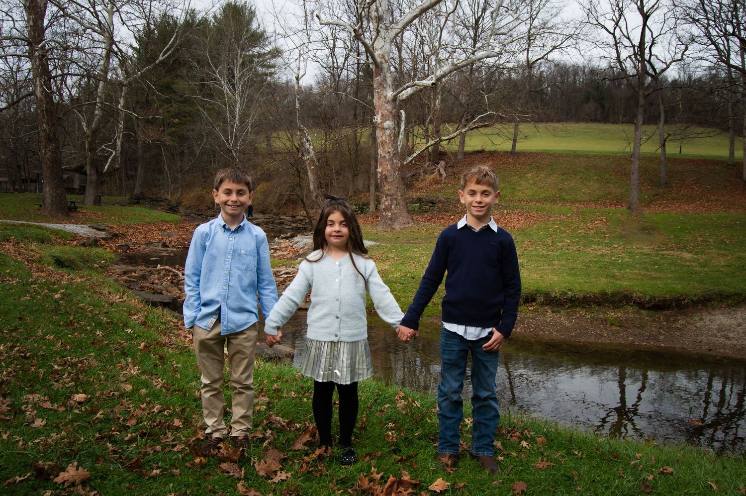 A group of people holding hands while standing in front of a pond on an autumn day.