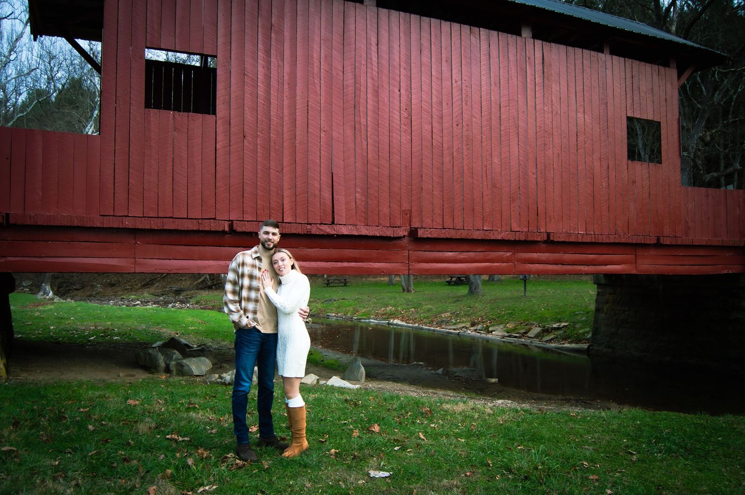 People enjoying a sunny day by a rustic red barn in a pastoral countryside setting.