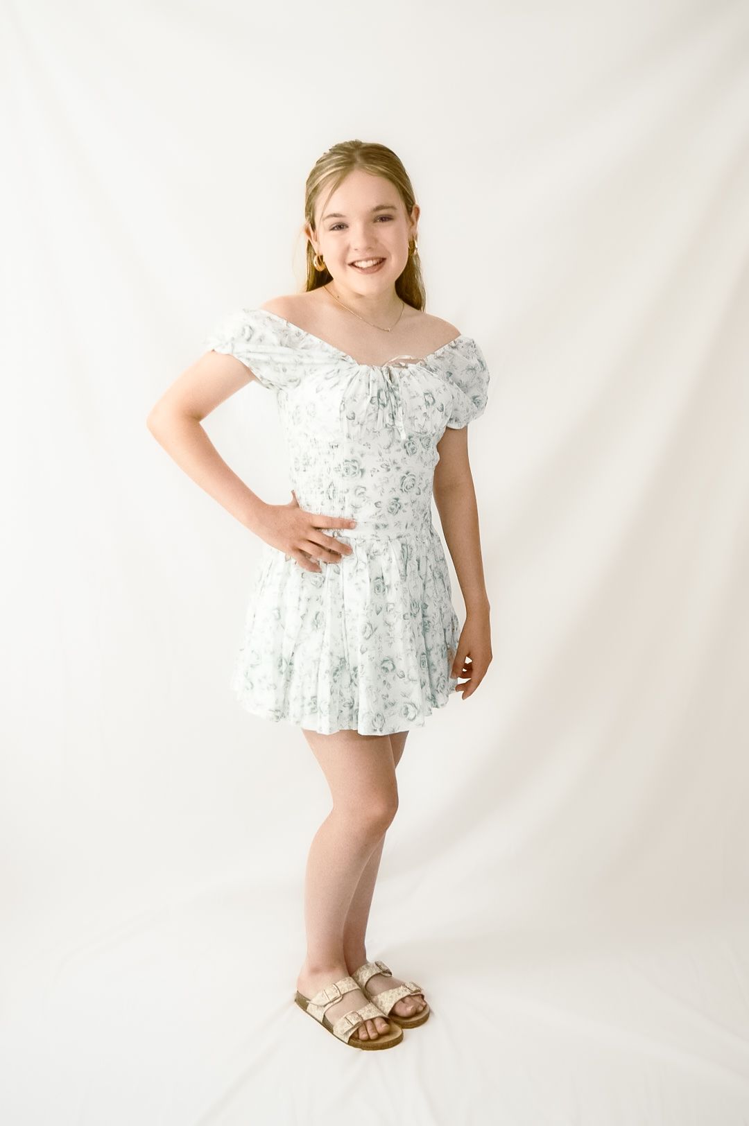 A series of four photos showing a child in a white floral dress and sandals posing against a light backdrop.