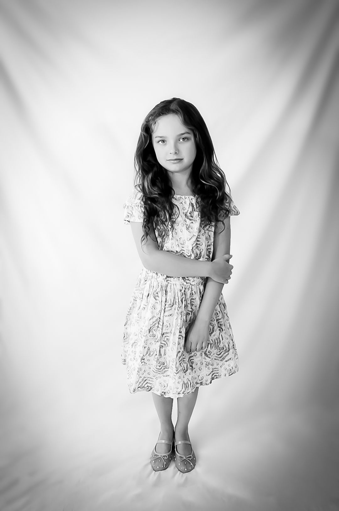Black and white artistic studio portrait series of a young child in a floral dress against a white backdrop.