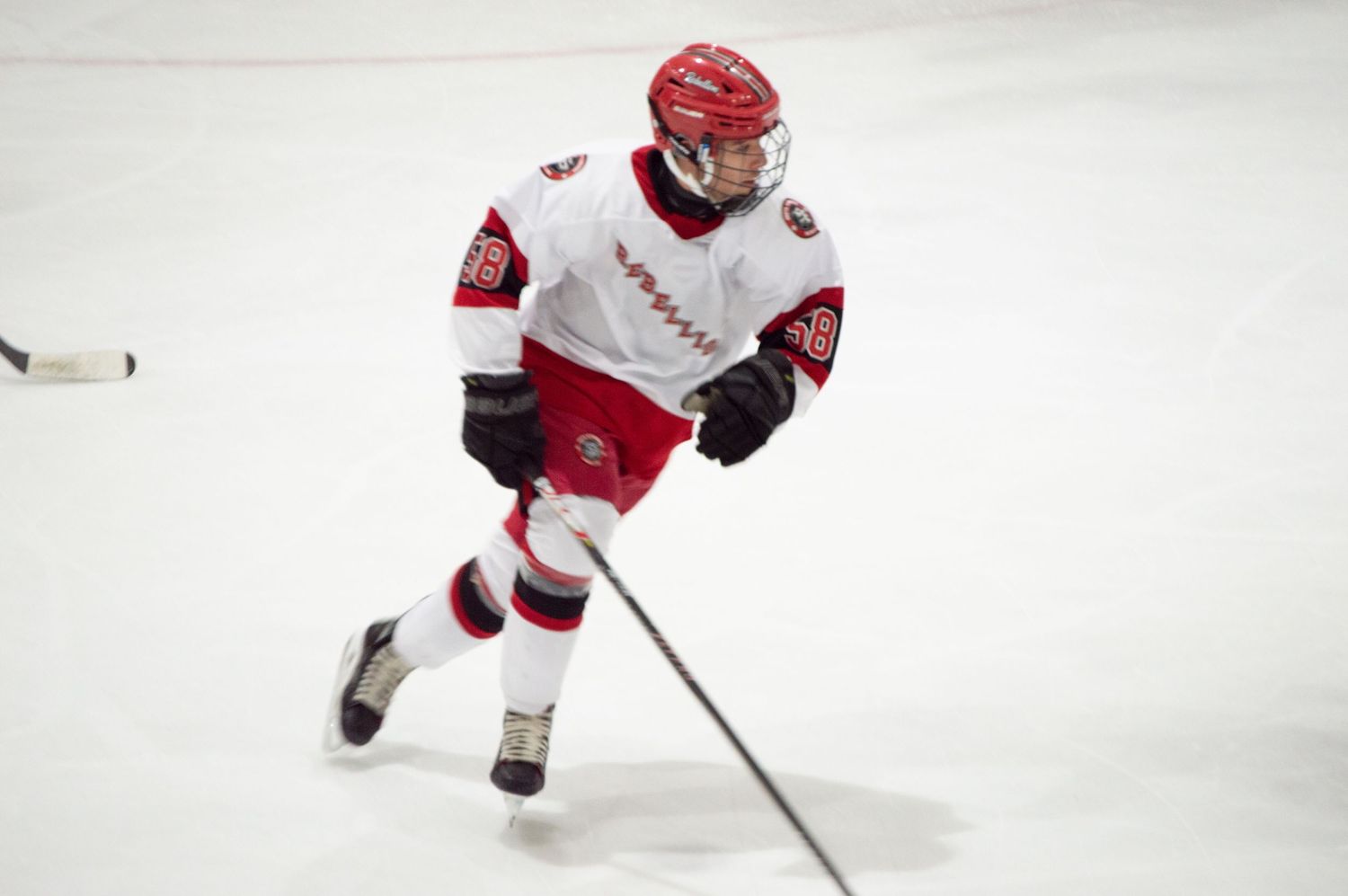 A hockey player in red and white uniform skates with the puck during an ice hockey match.